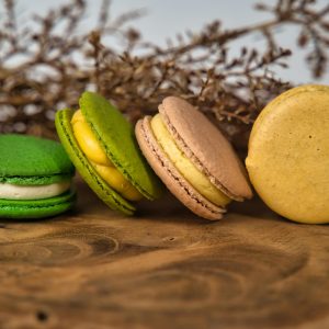 Elegant display of green, beige, and yellow macarons on wood with dried flowers in background.