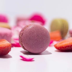 A close-up of a pink macaron surrounded by strawberries on a white surface.
