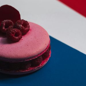 Close-up of a pink macaron topped with raspberries on a tricolor background.